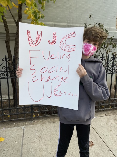 Child holds sign saying "UJC Fueling Social Justice"
